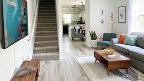 A modern living room with a staircase leading to a kitchen and dining area. - Sanctuary at Oaks | Full Kitchen • Near I75 (Gainesville)