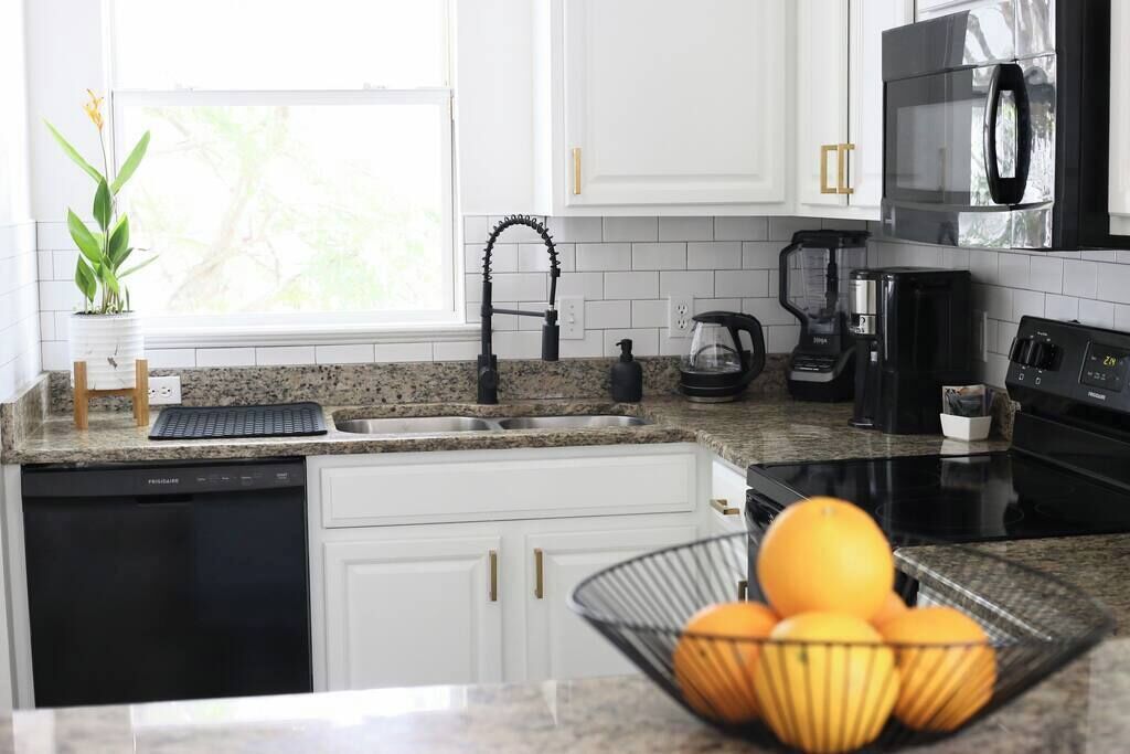 A modern kitchen with white cabinets, a granite countertop, a black dishwasher, a coffee maker, a kettle, and a microwave.