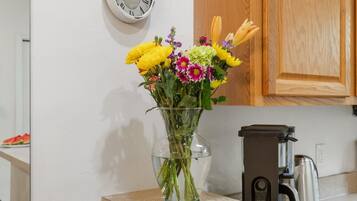 A kitchen with a clock on the wall, a coffee maker, and a vase with flowers on the counter.