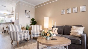 A living room with striped armchairs, a round coffee table with flowers, a sofa with patterned cushions, and wall art.