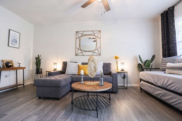 A modern living room with a sectional sofa, a round coffee table, and a bed.
