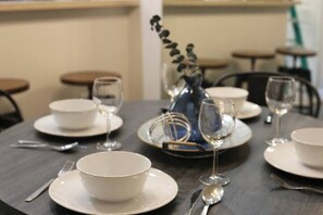 A dining table set with white plates, bowls, cutlery, and wine glasses, with a vase of flowers in the center.
