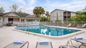 A swimming pool with lounge chairs and a covered area, surrounded by a fenced property.