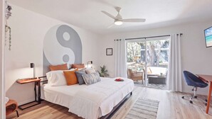A bedroom with a bed, a desk, a chair, a large window, and a ceiling fan. - The YinYang | King Bed • Workspace • Full Kitchen (Gainesville)