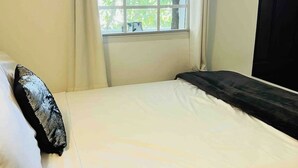 A bed with white bedding, a window with curtains, and a painting on the wall.