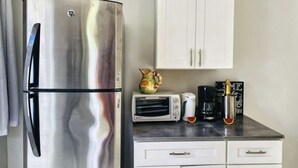 A compact kitchen with a stainless steel refrigerator, a microwave, a toaster, and a coffee maker on the countertop.