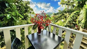 A balcony with a table and chairs, surrounded by lush greenery and a clear sky.