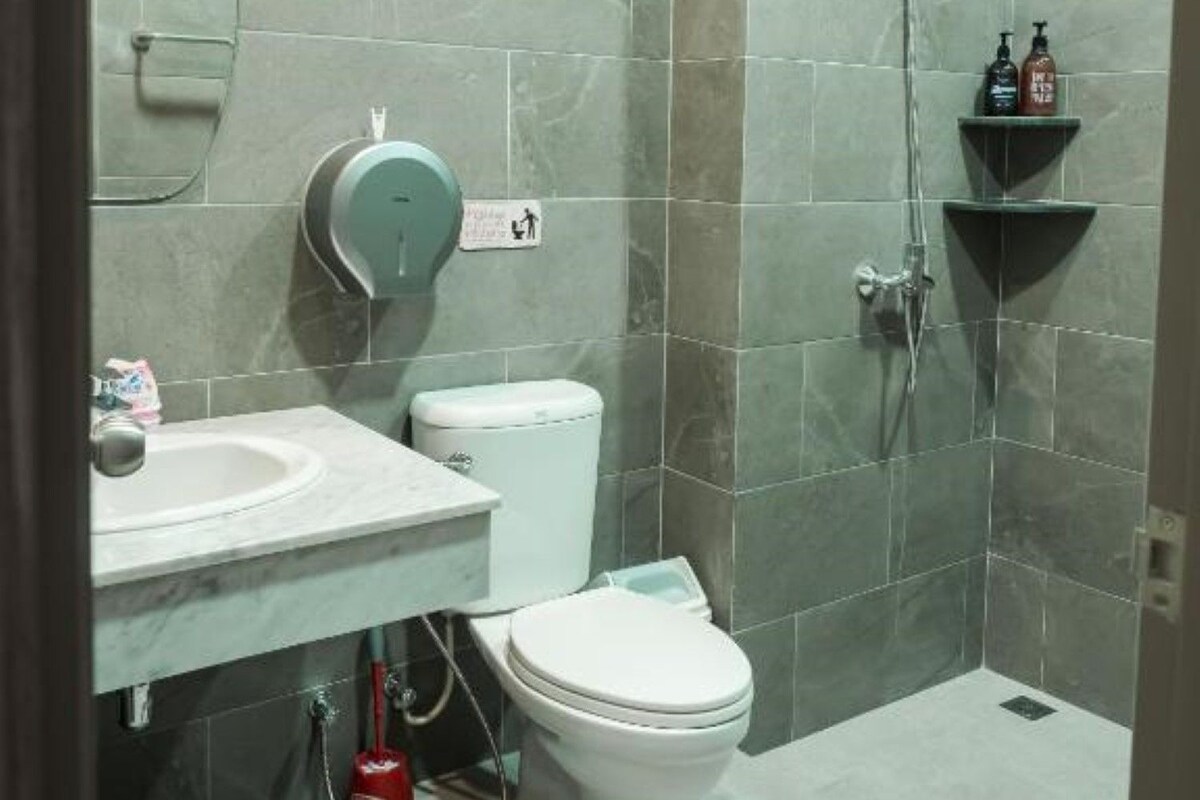 A modern bathroom with grey tiles, a white toilet, a sink, and a shower area.