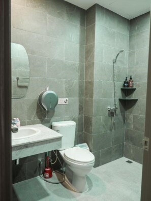 A modern bathroom with grey tiles, a white toilet, a sink, and a shower area. - Ray Hostel by Zuzu (Chiang Mai)
