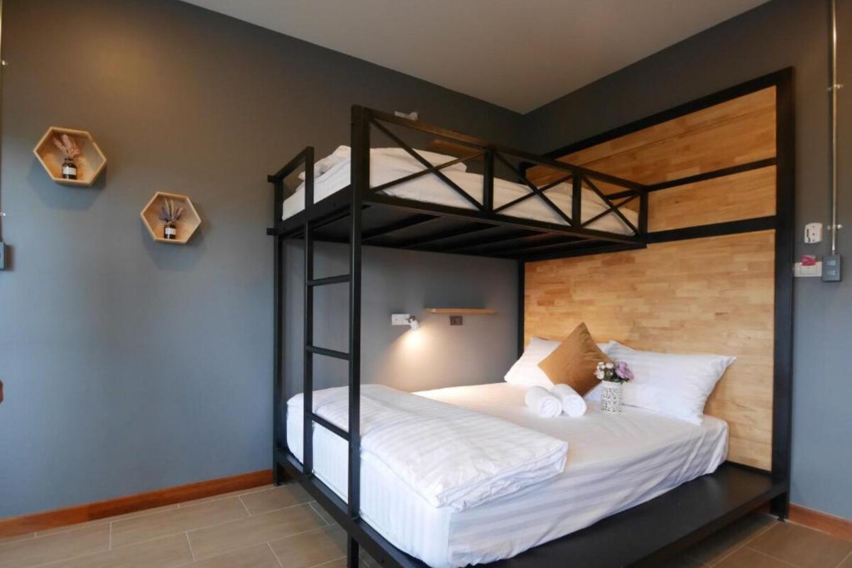A bunk bed room with a wooden headboard, a bedside table with a lamp, and two hexagonal shelves with decorative items.