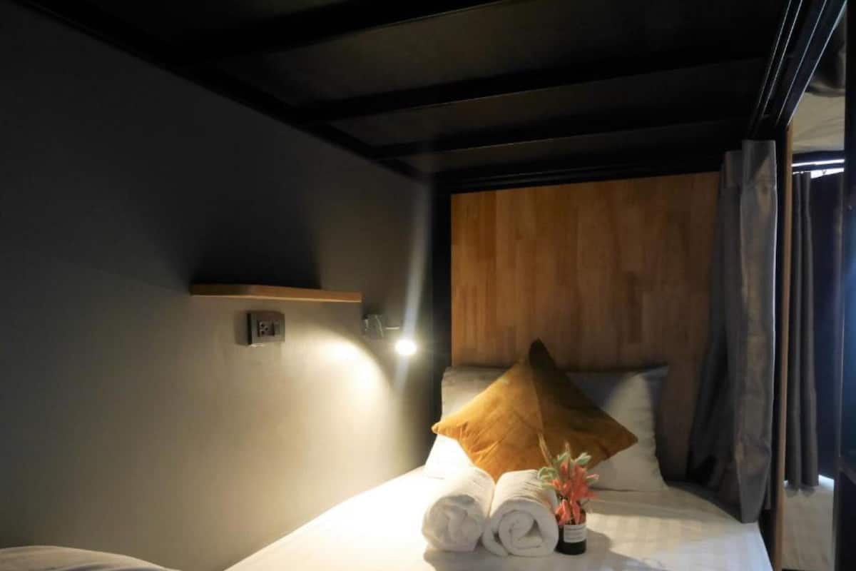 A hotel room with a bed, a wooden headboard, a wall-mounted light, and a window with curtains.
