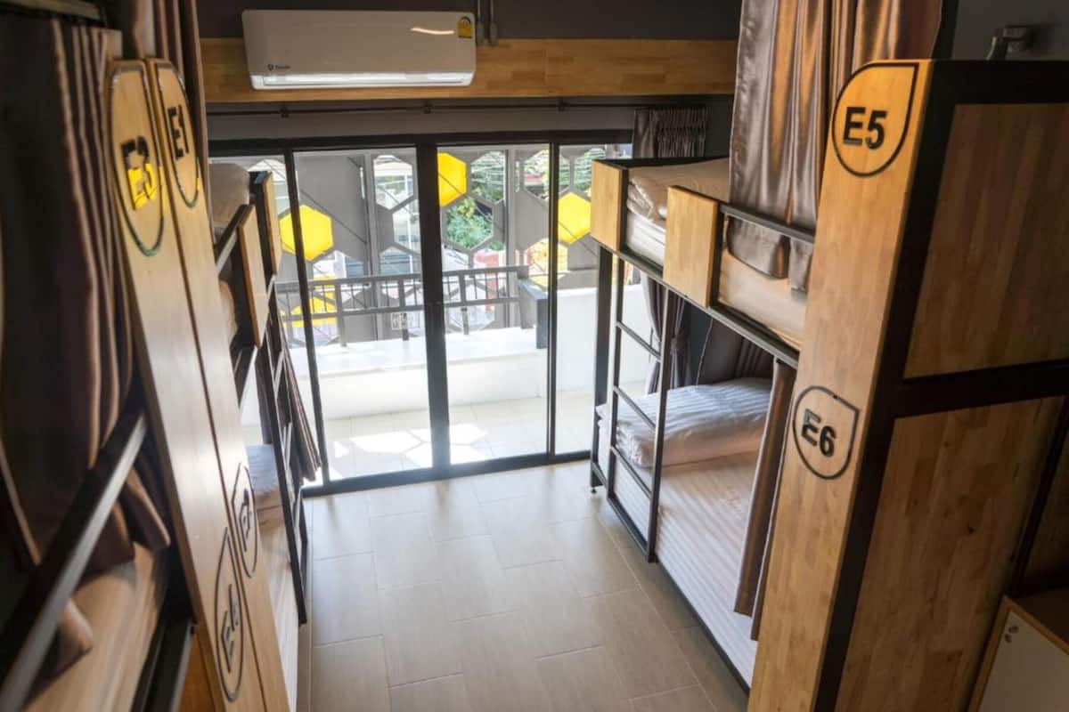 A dormitory room with bunk beds labeled E5 and E6, wooden walls, a window, and a view of the outside.