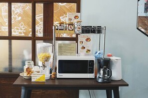 A breakfast setup with a microwave, coffee maker, and a menu on a table. - Ray Hostel by Zuzu (Chiang Mai)