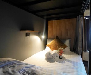 A hotel room with a bed, a wooden headboard, a wall-mounted light, and a window with curtains. - Ray Hostel by Zuzu (Chiang Mai)