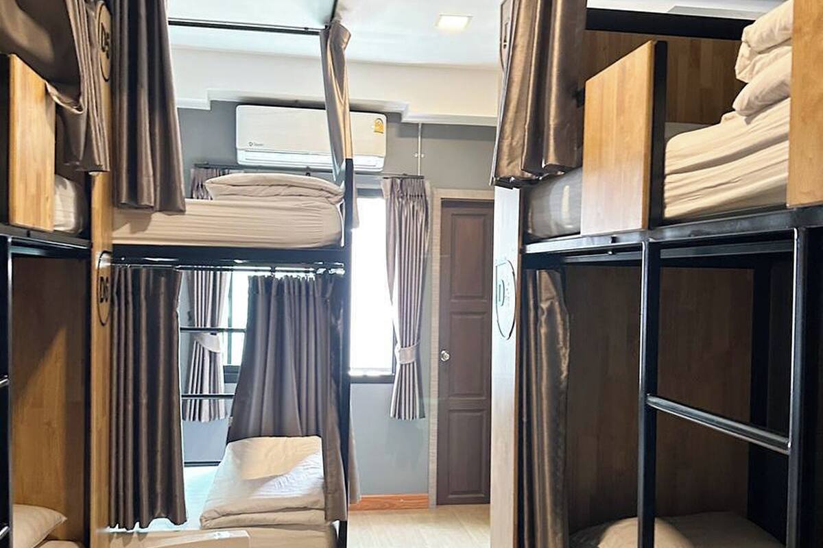 A dormitory room with bunk beds, a heater, and a window with curtains.