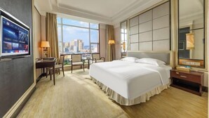 Une chambre d’hôtel avec un grand lit, un bureau, une chaise, une télévision et une vue sur la ville.