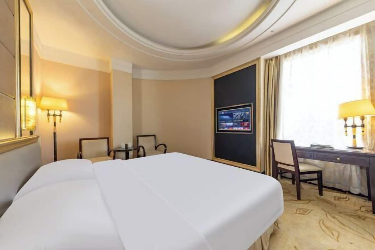 A hotel room with a large bed, a desk, a chair, a television, and a window with curtains.