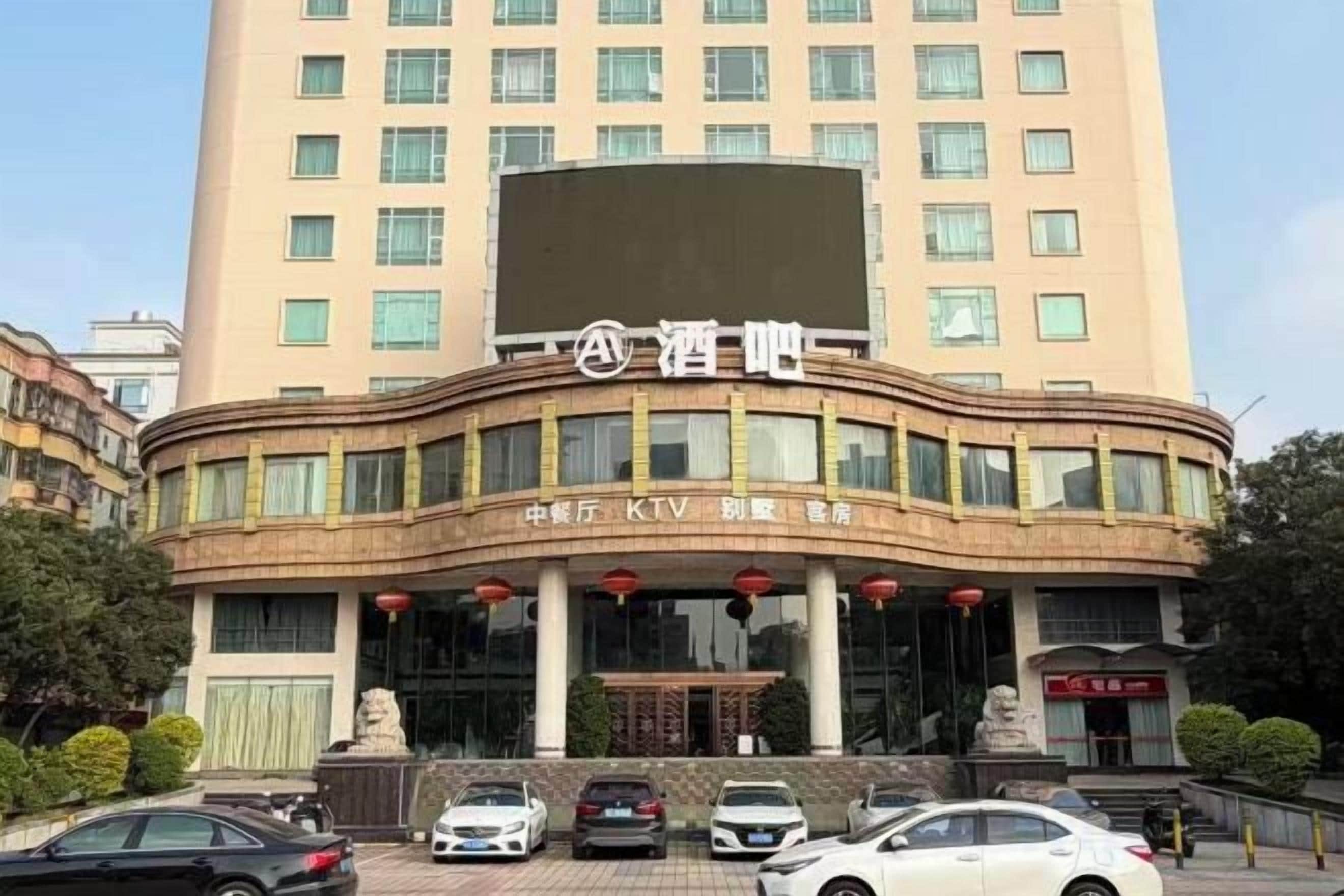 A hotel building with a prominent sign, multiple windows, and a parking area with several cars.