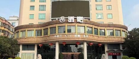 A hotel building with a prominent sign, multiple windows, and a parking area with several cars.