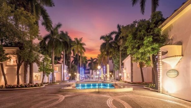 L’entrée d’un hôtel, avec une fontaine, des palmiers et un ciel au coucher du soleil.