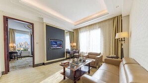 Une chambre d’hôtel avec un canapé, une table basse, une télévision et une vue sur la ville.
