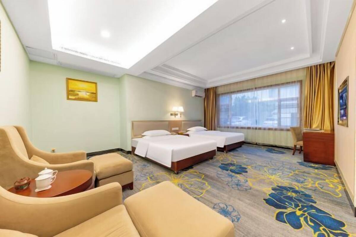 A hotel room with two beds, a sofa, a small table, and a large window with curtains.
