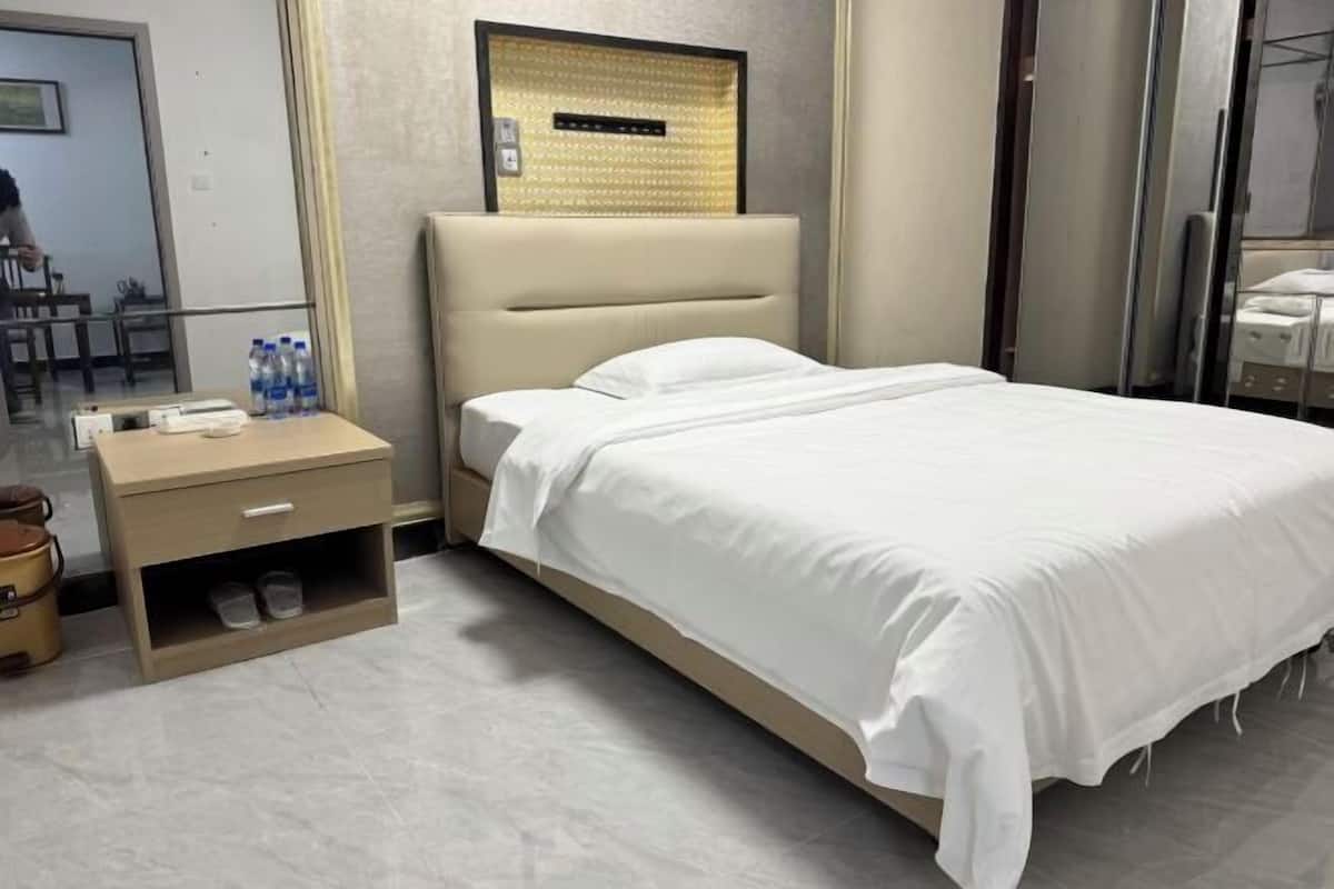 A hotel room with a bed, a nightstand, a mirror, and a wall-mounted light fixture.