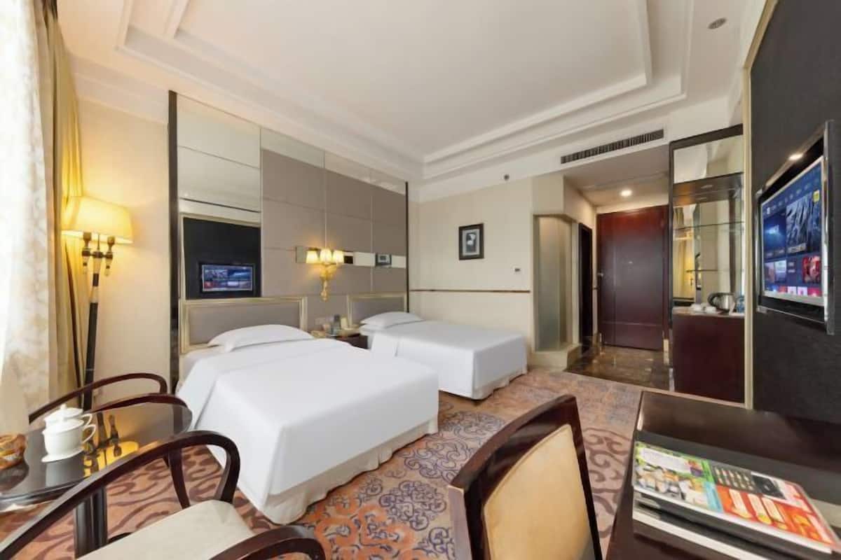A hotel room with two beds, a TV, a desk with a chair, and a minibar.