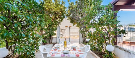 An outdoor dining area with a table set for two, surrounded by greenery and a clear sky.