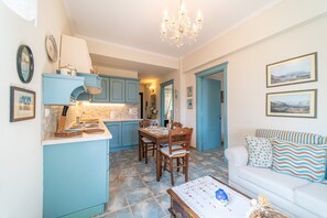 A kitchen with blue cabinets, a dining table with chairs, a white sofa with patterned cushions, and a chandelier.