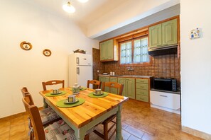 A dining area with a wooden table and chairs, a refrigerator, a microwave, and green cabinets.