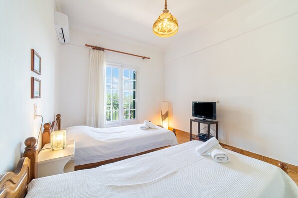 A hotel room with two beds, a television, a window with curtains, and a chandelier.