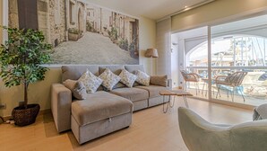 Un salón moderno con un sofá grande, una planta en maceta y vistas a un balcón con mobiliario exterior.