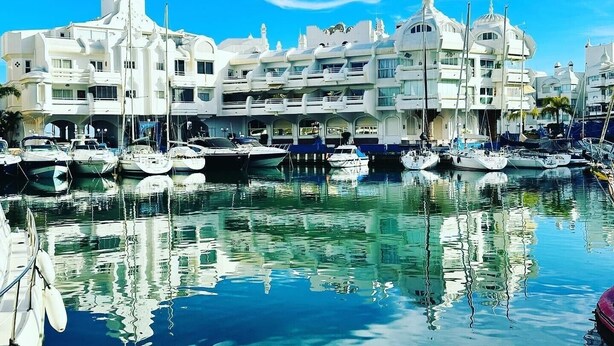 Un puerto deportivo con varias embarcaciones amarradas, rodeado de edificios blancos con balcones.