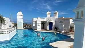Una piscina con agua azul cristalina, rodeada de edificios blancos con techos abovedados y una puerta azul.