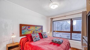 Una camera da letto con un'ampia finestra, una coperta rossa e un quadro colorato appeso al muro.
