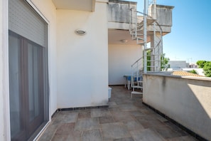 Un balcon étroit avec une porte coulissante, un escalier en métal et une petite table avec des chaises.