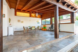 Un patio couvert comprenant une table et des chaises, des poutres en bois et un ventilateur de plafond.