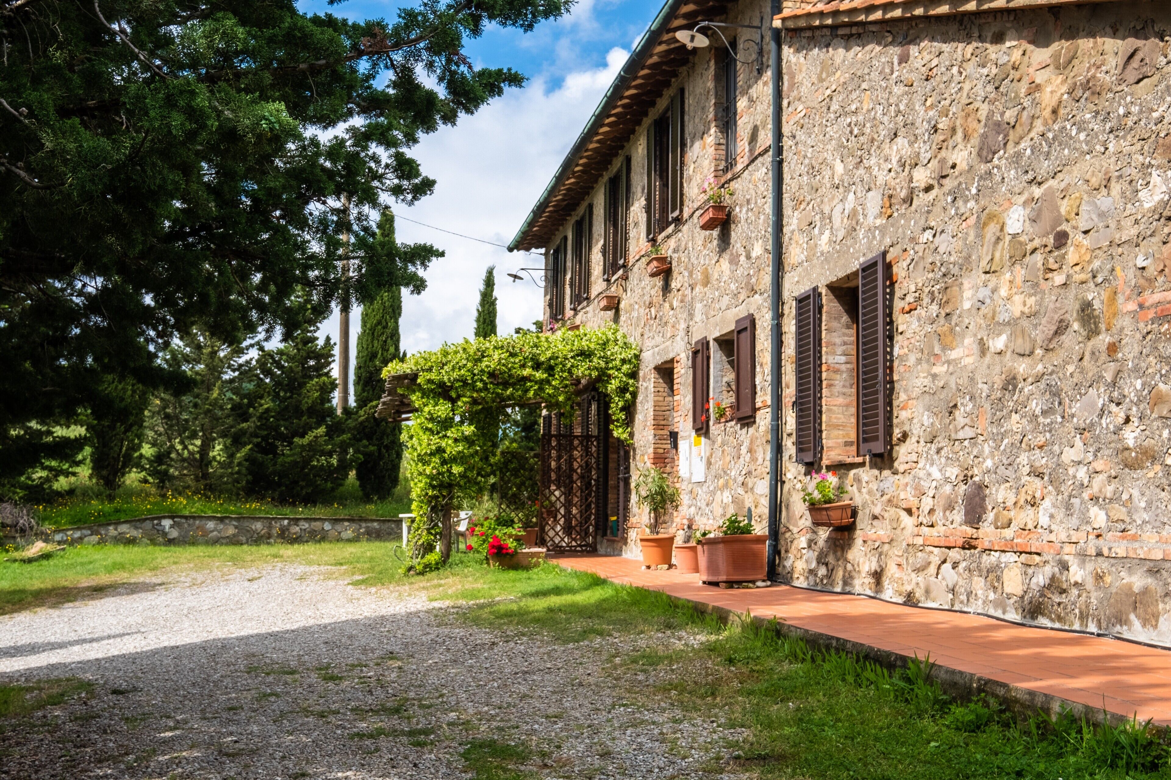 A stone building with a gravel path, potted plants, and a wooden fence.
