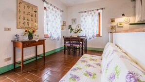 Ein Zimmer mit Holztisch, Stühlen, einer Couch, einem blumenmusterbett und einer Wandleuchte.