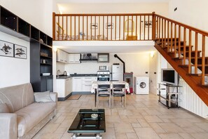 A spacious living area with a sofa, a coffee table, a kitchen with a stove, microwave, and washing machine, and a wooden staircase.
