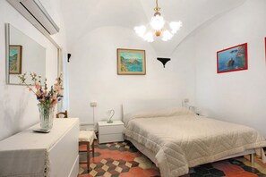 Un dormitorio con cama, mesita de noche, espejo, un florero con flores y una pared con dos cuadros enmarcados.