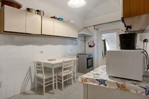 Una cocina con armarios blancos, una mesa de comedor con sillas, un horno pequeño y un refrigerador.