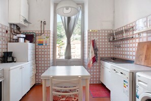 A compact kitchen with a dining table, chairs, a washing machine, and a window with curtains.