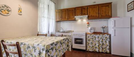 A kitchen with wooden cabinets, a stove, a refrigerator, and a table with a floral tablecloth.