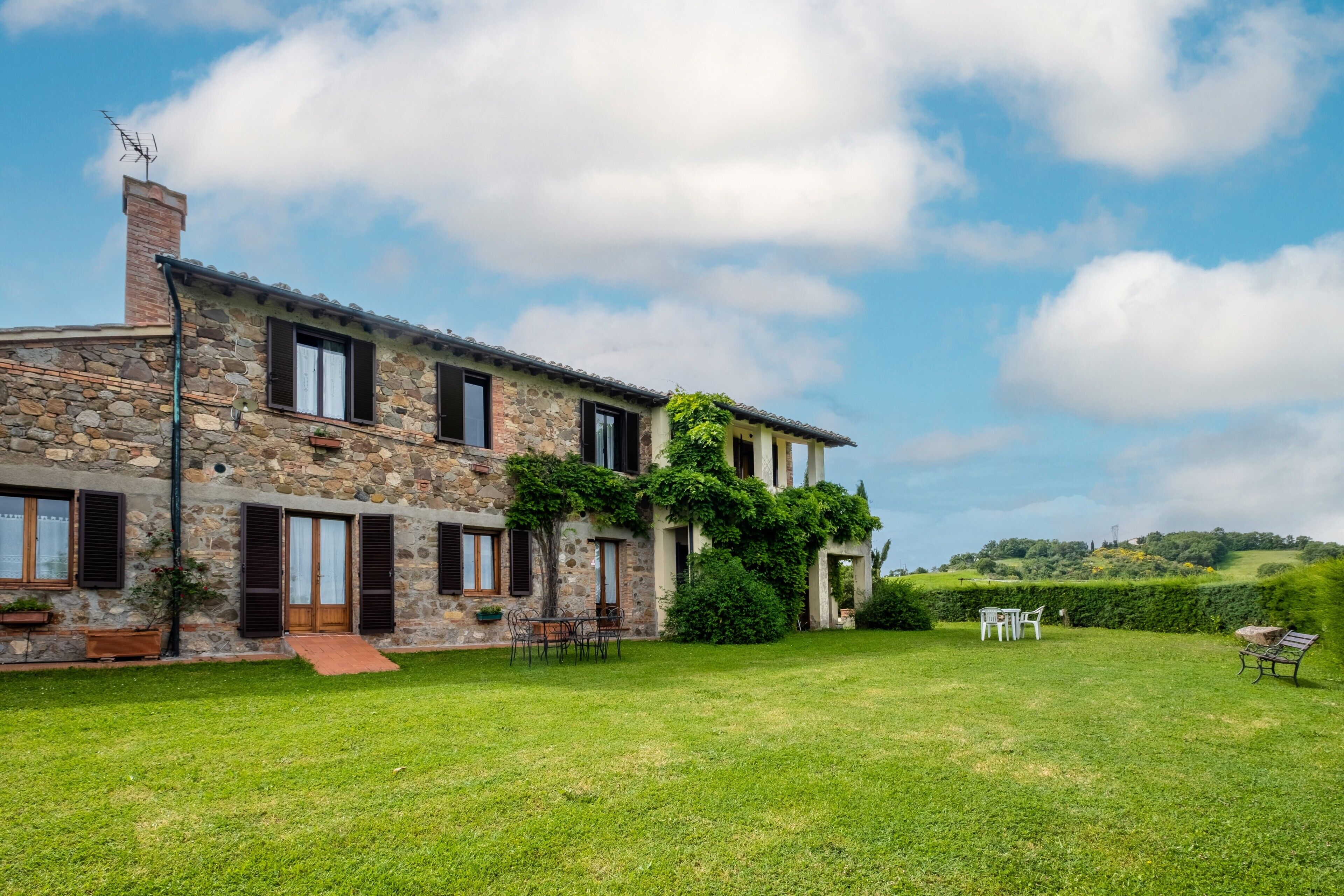 A stone house with a grassy yard, outdoor seating, and a clear sky.