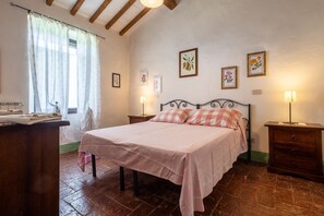 Ein Schlafzimmer mit einem Bett, zwei Nachttischen, einer Holzkommode, einem Fenster mit Vorhängen und gerahmten Bildern an der Wand.