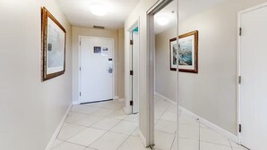 Un couloir avec une porte blanche, des tableaux encadrés accrochés aux murs et un sol carrelé.