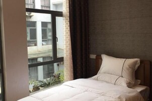 Habitación de hotel con un ventanal grande, una cama con ropa blanca y vistas a edificios.
