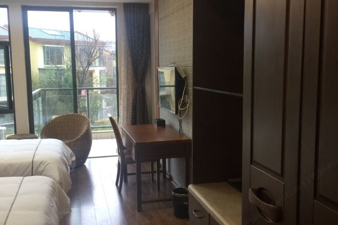 A hotel room with a bed, a desk, a chair, a television, and a window with a view of buildings outside.